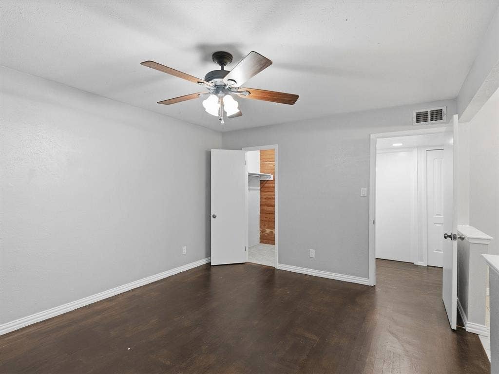 Room featuring wood-finish flooring, neutral wall paint, a multi-blade ceiling fan with integrated lighting, and a reach-in closet with shelving
