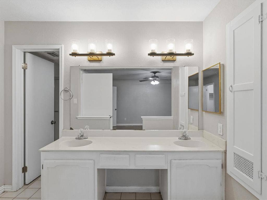 Double vanity featuring white cabinetry, a light-toned solid surface countertop with integrated dual sinks, two three-light fixtures, and a large plate glass mirror