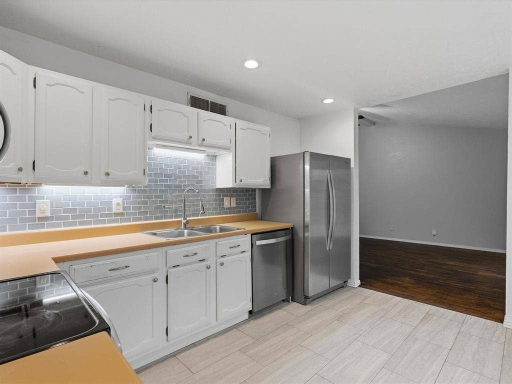 Kitchen featuring white cabinetry, stainless steel appliances, subway tile backsplash, solid-surface countertops, and tile flooring