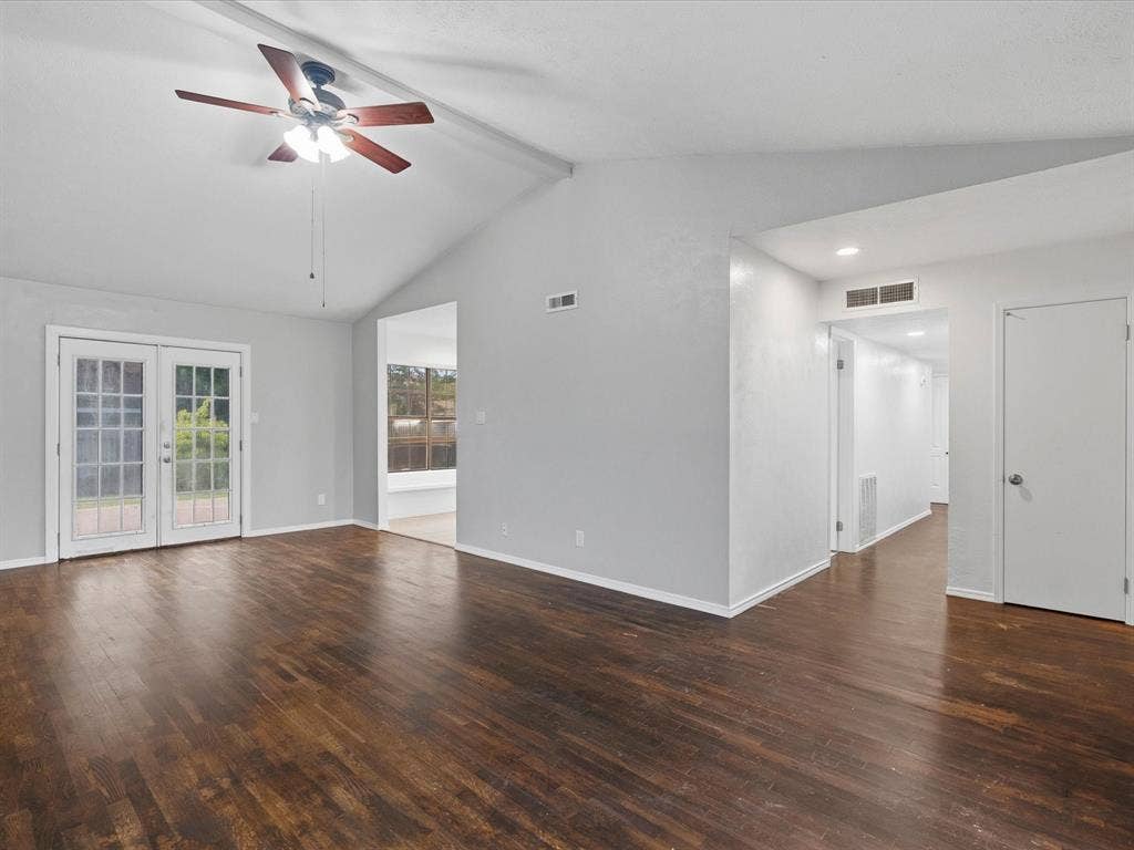 Vaulted ceiling featuring a central ceiling fan with multi-light fixture, wood-finish flooring, and glass-paneled double doors