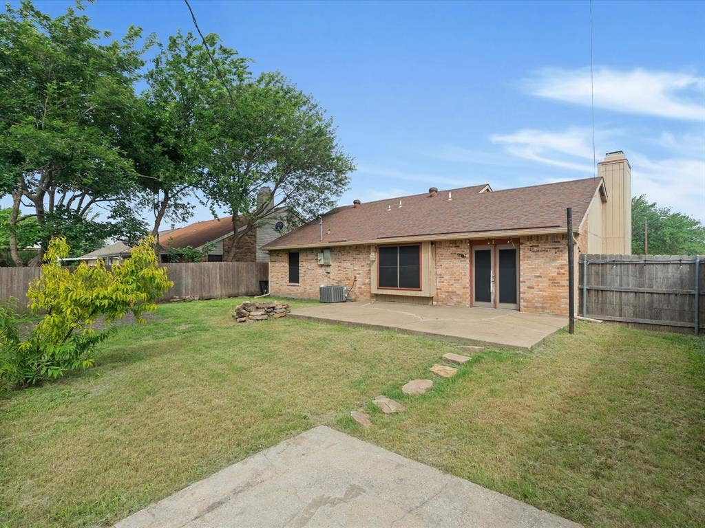 Backyard featuring a concrete patio, stone stepping path, brick exterior, chimney, and wood perimeter fencing