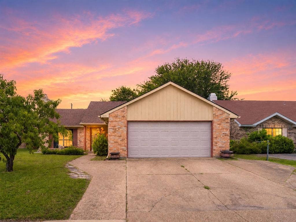 Single-story exterior featuring a brick facade, vertical siding, an attached two-car garage, and concrete driveway