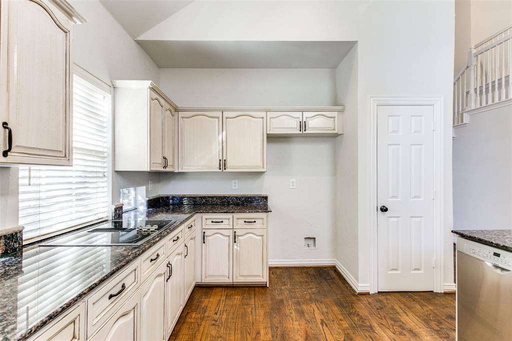 1214 Saint Regis Drive, Irving, TX 75038 Kitchen featuring vaulted ceilings, wood-finish flooring, dark stone countertops, off-white cabinetry with matte black hardware, and stainless steel integrated dishwasher