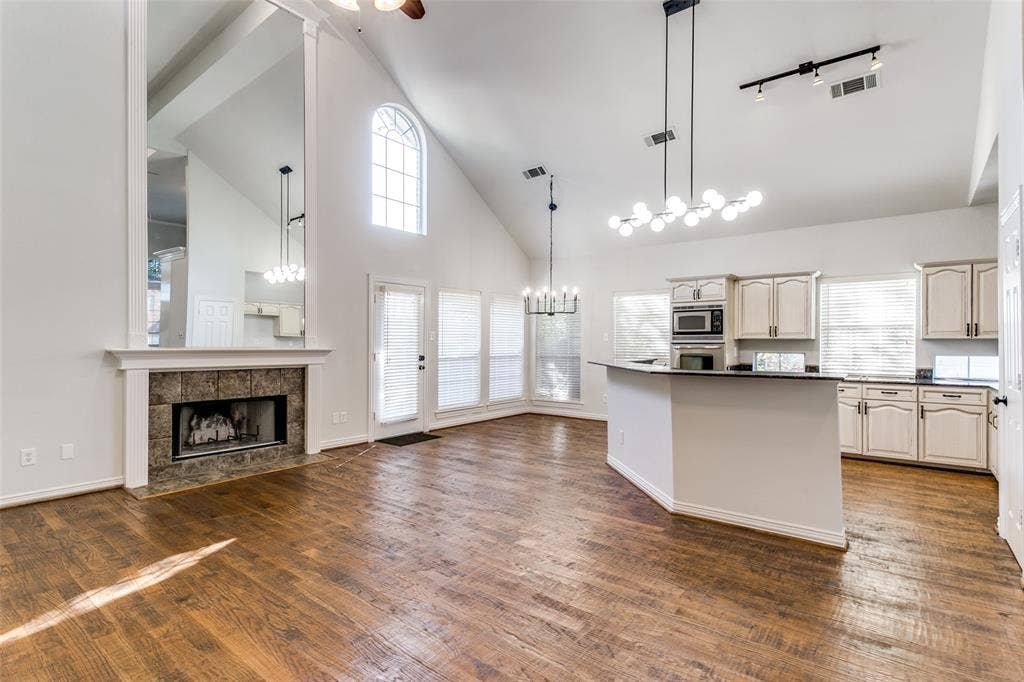 1214 Saint Regis Drive, Irving, TX 75038 Vaulted ceilings, wood-finish flooring, stone-surround fireplace with floor-to-ceiling mirror, arched window, and custom kitchen cabinetry with integrated stainless steel appliances