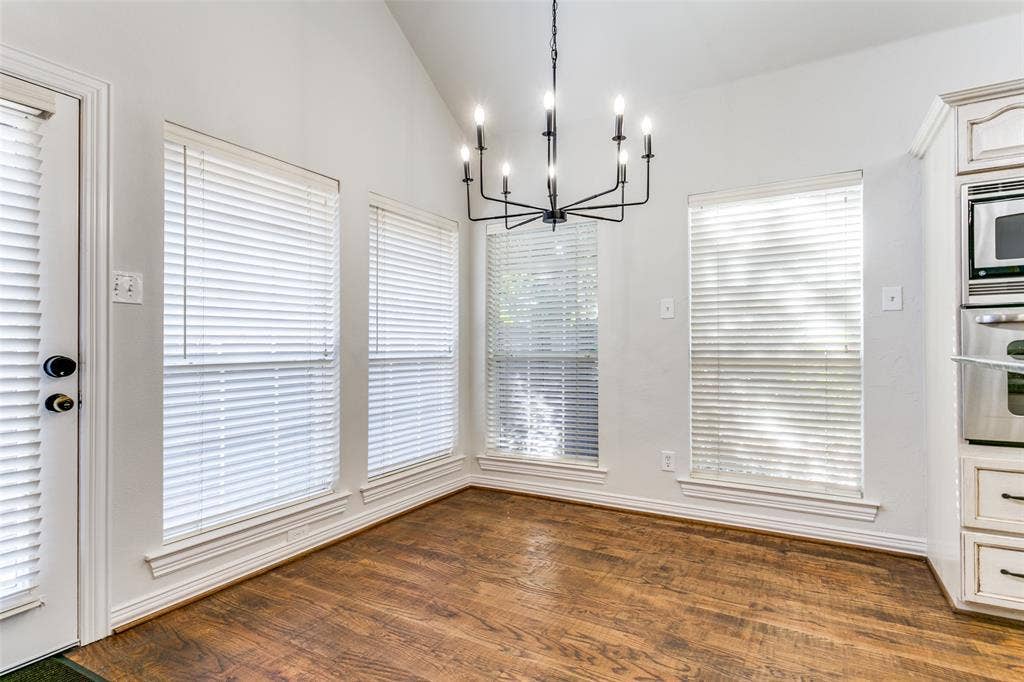 1214 Saint Regis Drive, Irving, TX 75038 Vaulted ceiling featuring a multi-arm iron chandelier, wood-finish flooring, and multiple windows with horizontal blinds