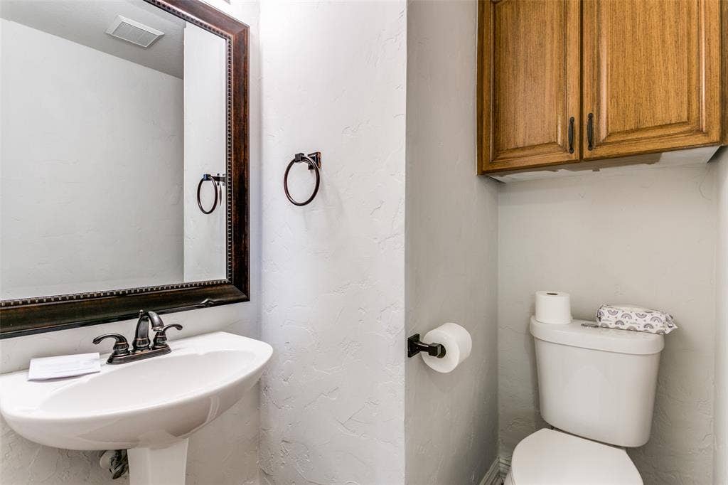1214 Saint Regis Drive, Irving, TX 75038 Wall-mounted wood-finish cabinetry, pedestal sink with dual-handle metal faucet, and framed wall mirror with coordinating metal hardware