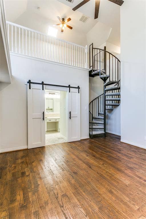 1214 Saint Regis Drive, Irving, TX 75038 Vaulted ceilings featuring a black metal spiral staircase, wood-finish flooring, white sliding barn doors with matte black hardware, and an open balcony with a white railing
