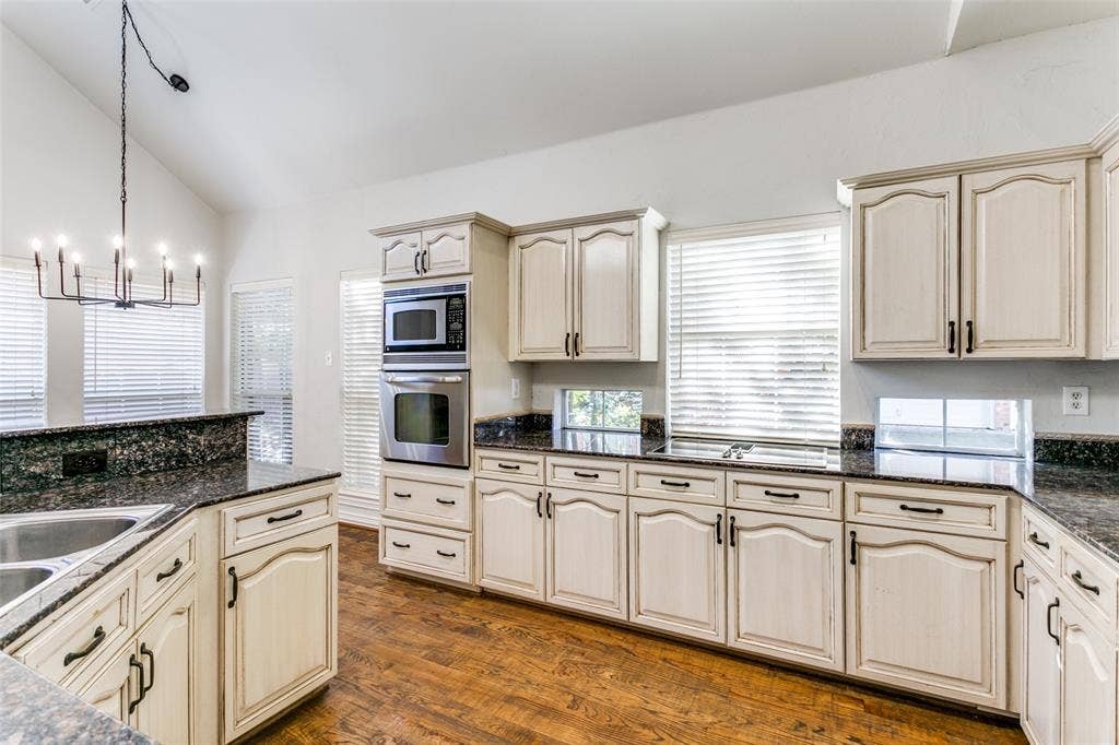 1214 Saint Regis Drive, Irving, TX 75038 Kitchen featuring wood-finish flooring, stone countertops, double wall ovens, cabinetry with arched-panel detailing, and a vaulted ceiling with an iron chandelier