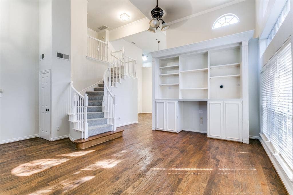 1214 Saint Regis Drive, Irving, TX 75038 Living area featuring wood-finish flooring, a vaulted ceiling, a built-in floor-to-ceiling white bookshelf with cabinetry, a curved staircase with white railings, and an arched transom window