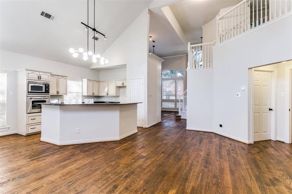 1214 Saint Regis Drive, Irving, TX 75038 Open-concept interior featuring vaulted ceilings, wood-finish flooring, a kitchen island with stone countertops, built-in stainless steel appliances, and an elevated wooden staircase with white balusters