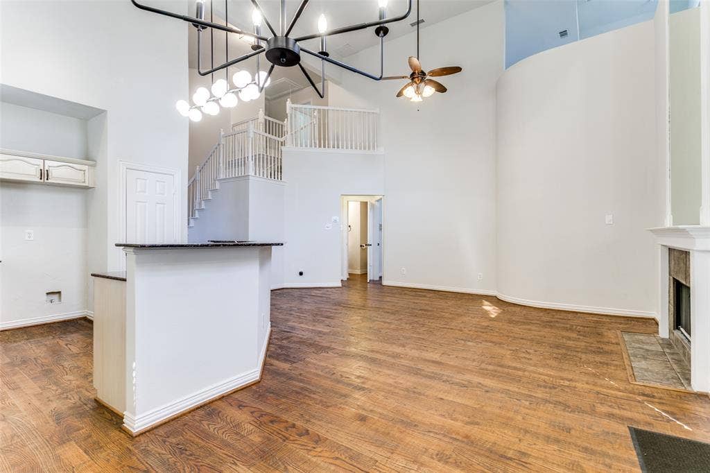 1214 Saint Regis Drive, Irving, TX 75038 Open concept living area featuring vaulted ceilings, wood-finish flooring, a tiered staircase with white balusters, a built-in fireplace with stone hearth, and a multi-light chandelier