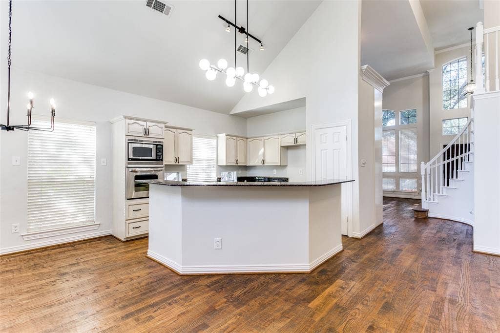 1214 Saint Regis Drive, Irving, TX 75038 Kitchen featuring wood-finish flooring, vaulted ceilings, stone-surfaced island countertop, built-in wall oven and microwave, and multi-light chandelier