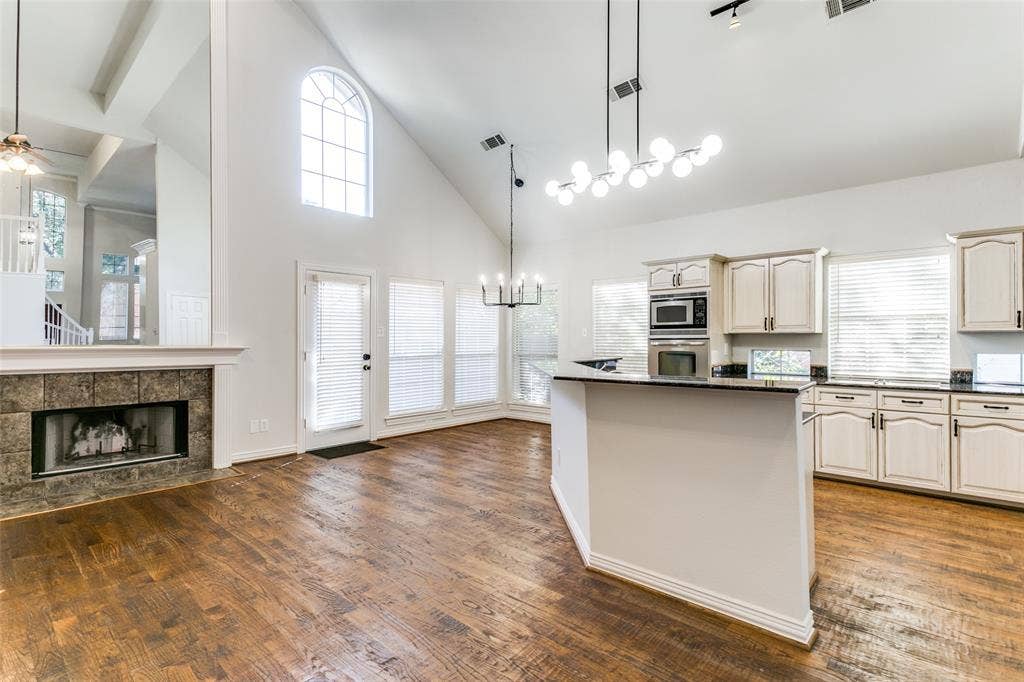 1214 Saint Regis Drive, Irving, TX 75038 Vaulted ceilings, wood-finish flooring, stone-surround fireplace, multi-light chandeliers, and cabinetry with integrated stainless steel appliances