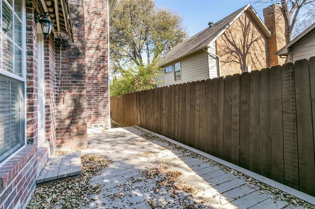 1214 Saint Regis Drive, Irving, TX 75038 Exterior side yard featuring a brick facade, concrete patio, and vertical wood fencing