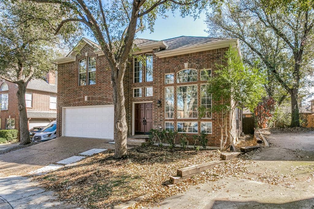 1214 Saint Regis Drive, Irving, TX 75038 Two-story brick exterior featuring an arched entryway, multi-pane windows, and an attached two-car garage