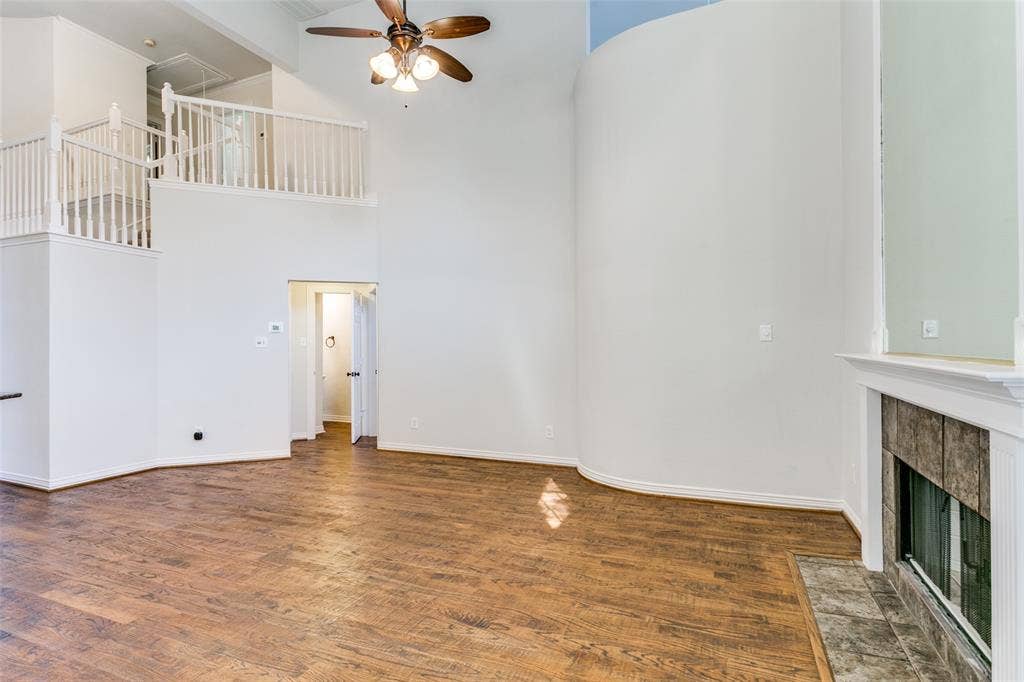 1214 Saint Regis Drive, Irving, TX 75038 High-ceiling interior featuring wood-finish flooring, a curved architectural wall, a fireplace with tile surround, and an elevated balustrade landing