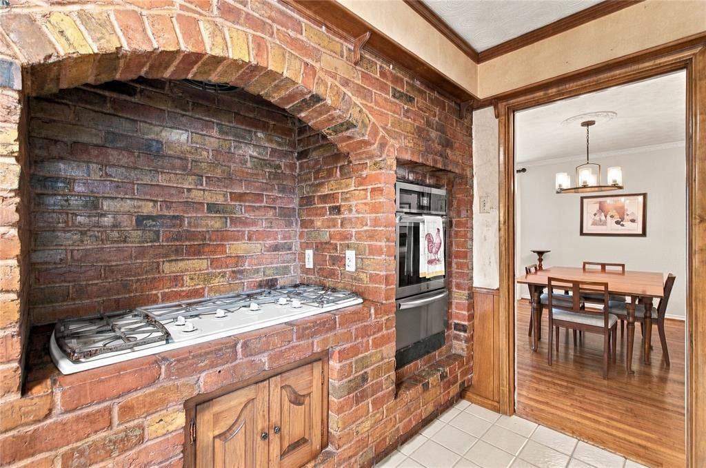 Exposed brick arched cooking alcove featuring a built-in gas cooktop, integrated stainless steel wall oven, and wood-paneled cabinetry