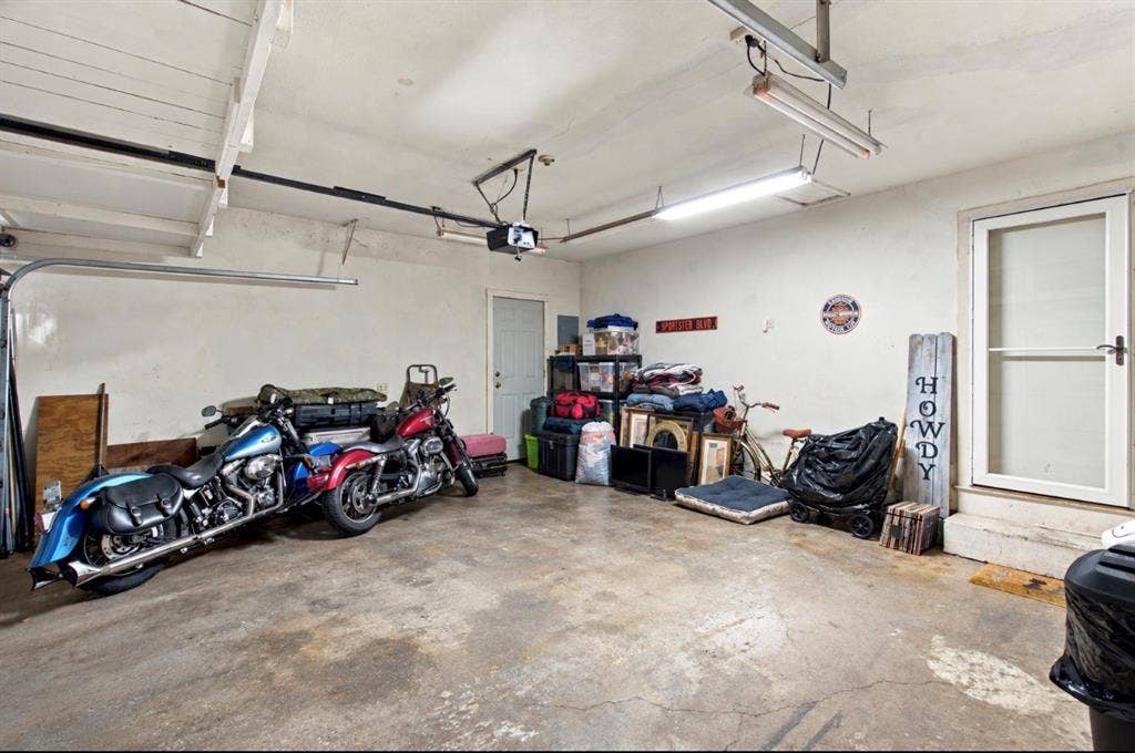 Garage interior featuring concrete flooring, overhead fluorescent lighting, and a walk-out utility door