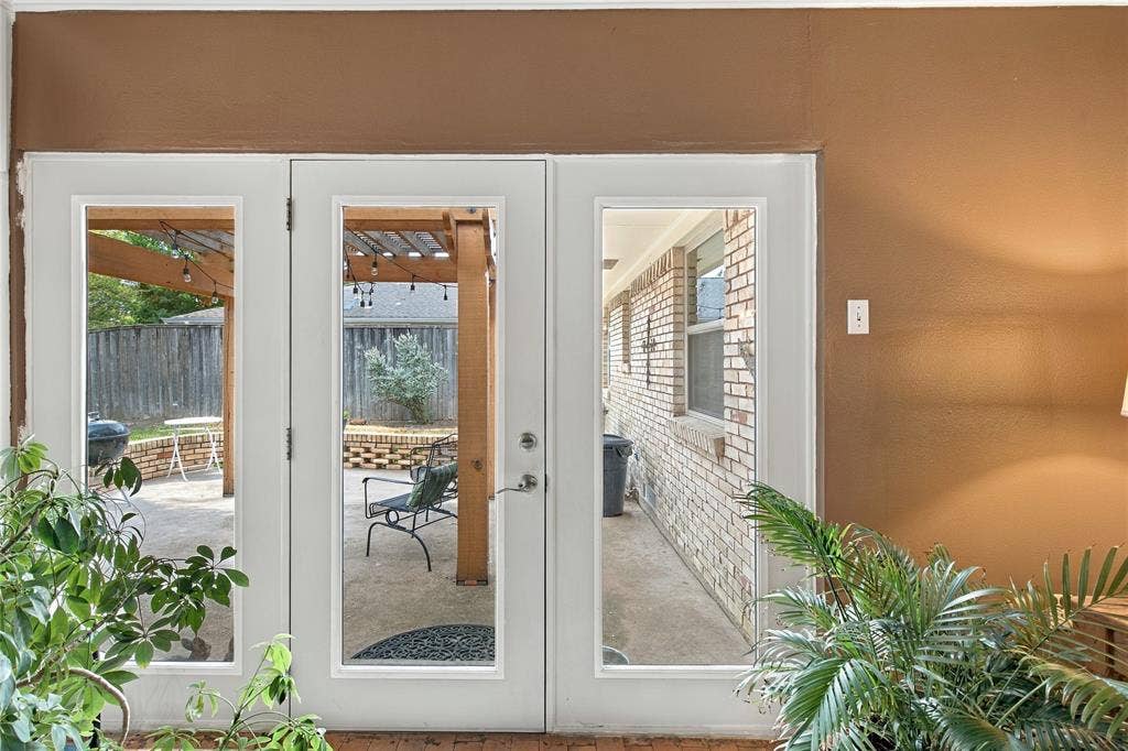 Glass-paned door system featuring dual sidelights and a brick exterior facade with an attached wooden pergola
