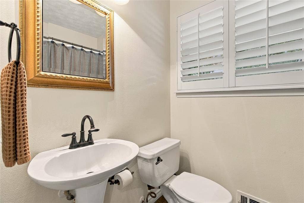 Pedestal sink with an oil-rubbed bronze faucet, decorative gold-toned framed mirror, and white plantation shutters