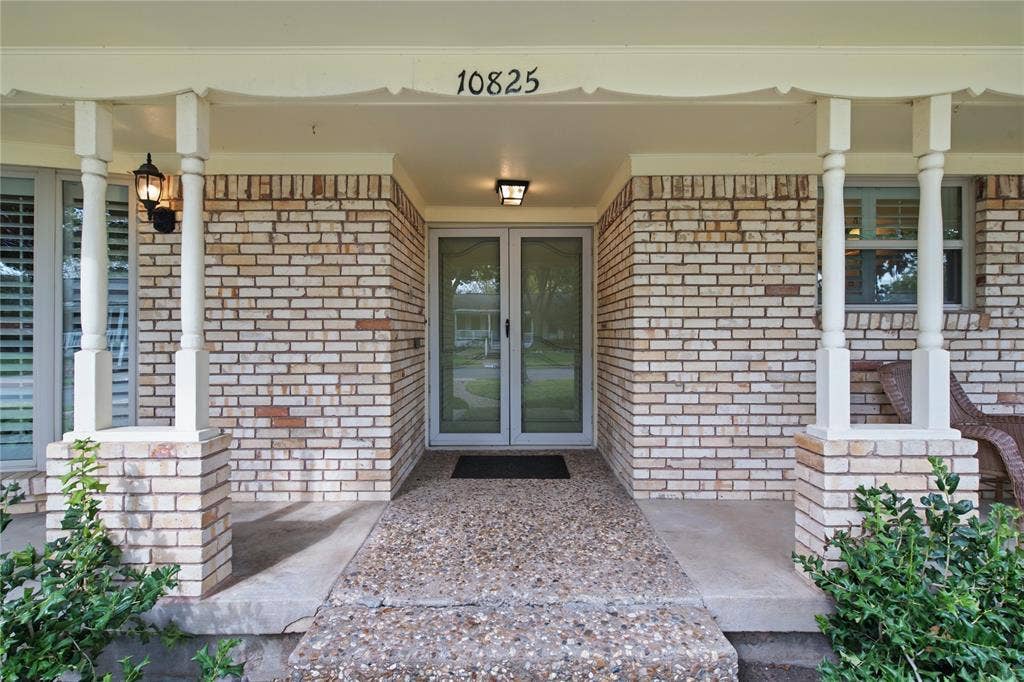 Covered front porch featuring light brick masonry, decorative turned wood columns, aggregate concrete flooring, and a double-glass entry door