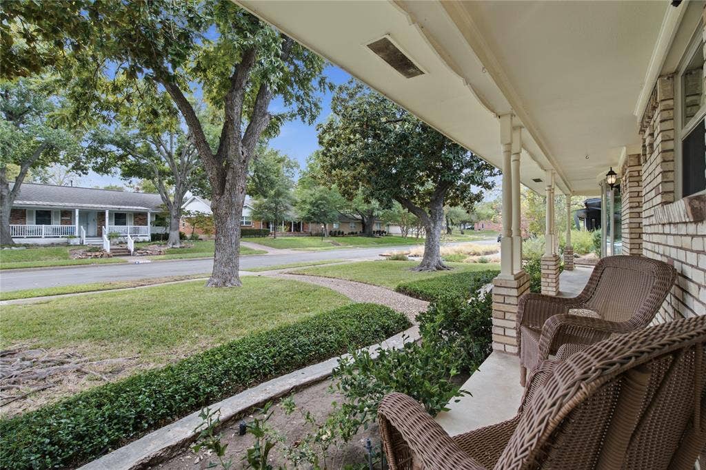 Covered front porch with brick column bases, concrete flooring, and exterior wall-mounted lighting