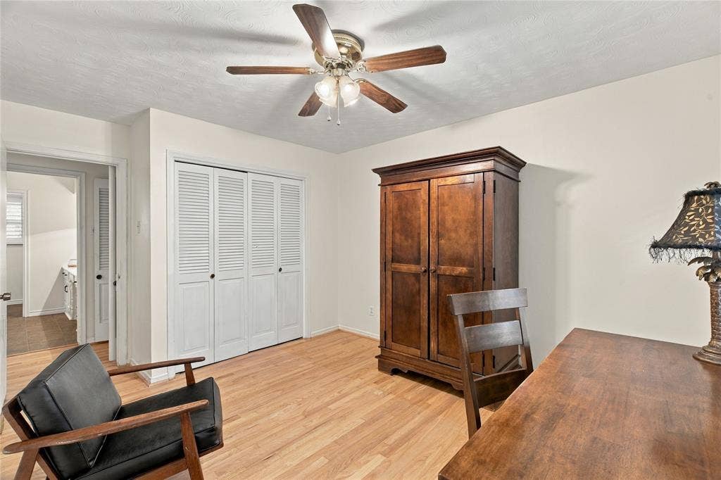 Wood-finish flooring, white louvered-style bi-fold closet doors, and a ceiling-mounted fan with integrated lighting