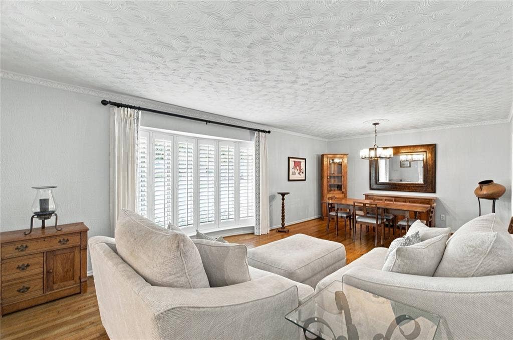 Bay window with integrated shutters, wood-finish flooring, ceiling with textured finish, and crown molding