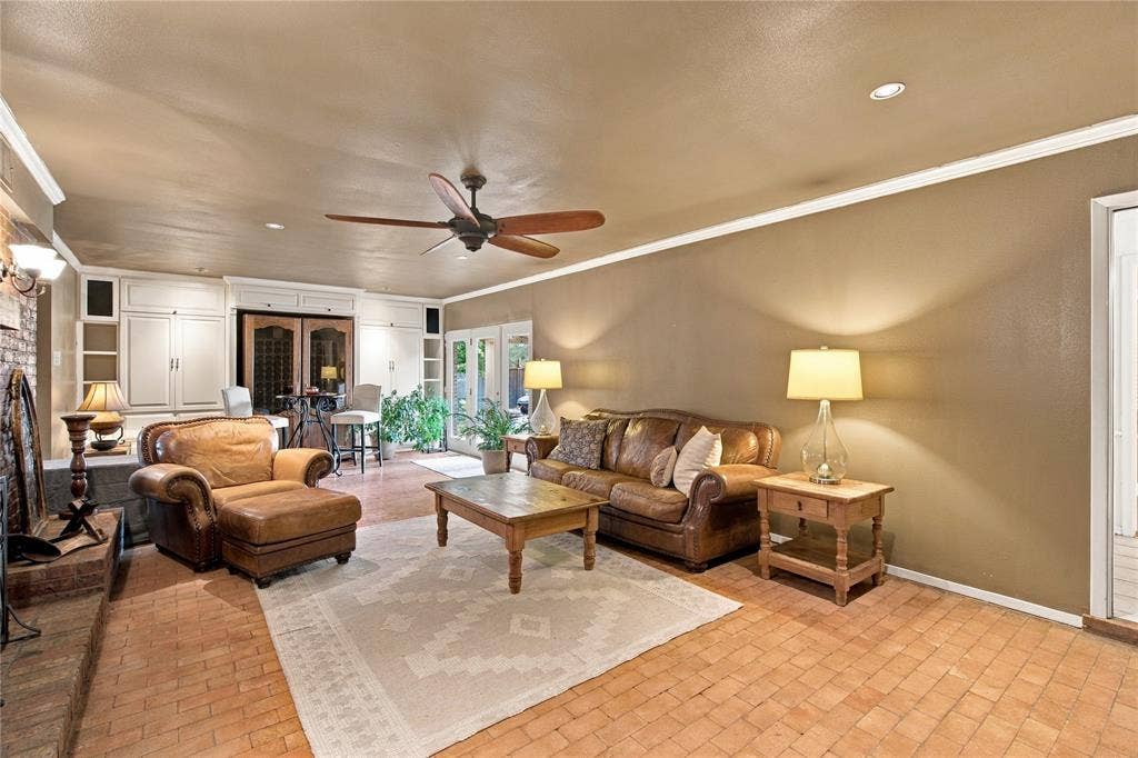 Interior space featuring terra-cotta tile flooring, a floor-to-ceiling brick fireplace, built-in cabinetry, and a ceiling fan