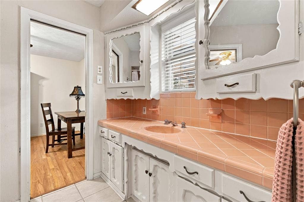 Custom white cabinetry with scalloped detailing, square tile countertop with integrated sink, matching tile backsplash, dual recessed medicine cabinets, and brushed metal hardware