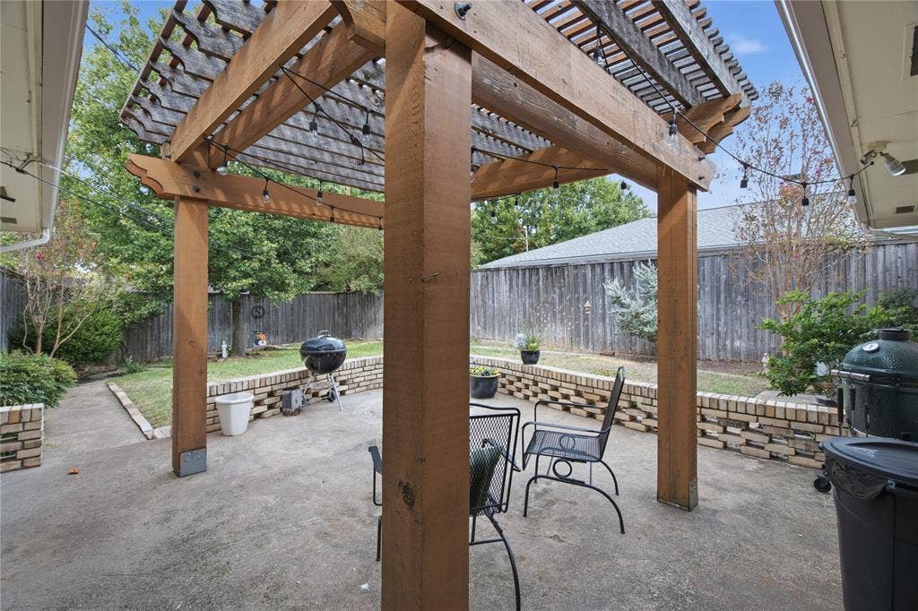 Backyard featuring a substantial wood pergola, concrete patio, perimeter brick retaining wall, and wood privacy fencing