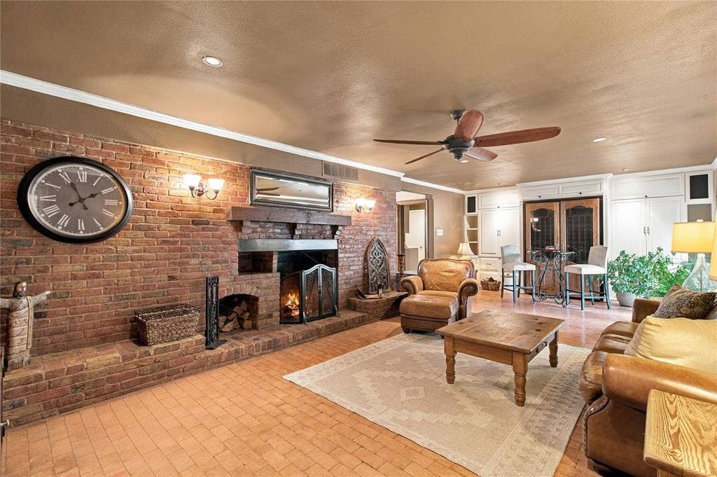 Exposed brick fireplace featuring a wood-beam mantel, tile flooring, built-in cabinetry, and a ceiling fan