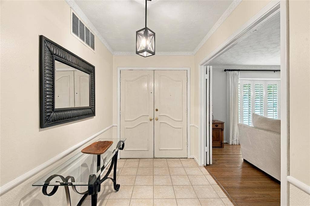 Foyer featuring double entry doors, tile flooring, crown molding, and a geometric pendant light fixture