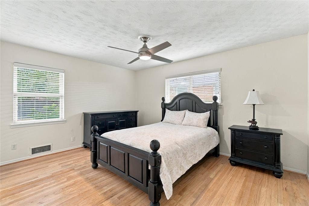 Room with light-toned wood-finish flooring, dual windows with blinds, and a central ceiling fan with integrated lighting