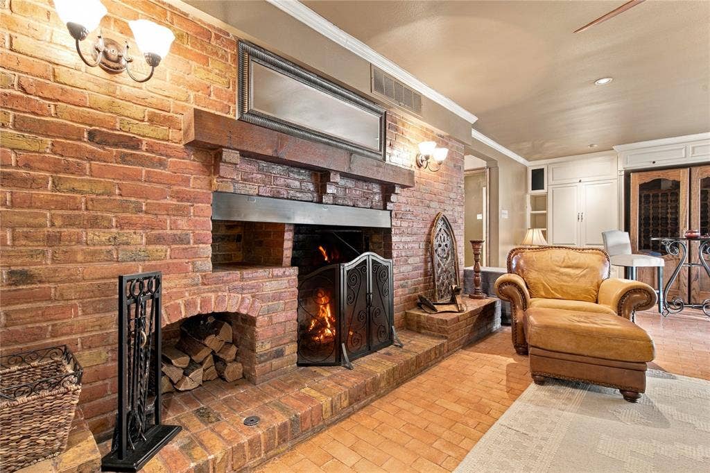 Exposed brick fireplace featuring a wood beam mantel, recessed storage nook, and raised brick hearth