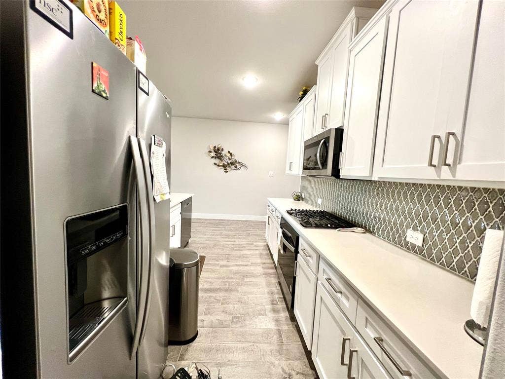 2707 Woodland Court, Wylie, TX 75098 Kitchen with stainless steel appliances, white cabinetry, light wood-type flooring, and tasteful backsplash