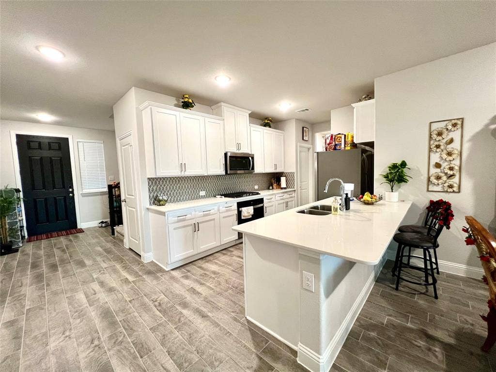 2707 Woodland Court, Wylie, TX 75098 Kitchen with sink, light hardwood / wood-style flooring, white cabinetry, appliances with stainless steel finishes, and a kitchen bar