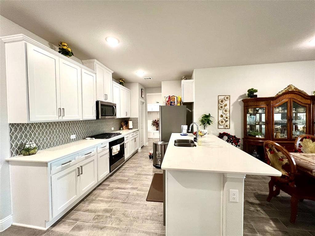 2707 Woodland Court, Wylie, TX 75098 Kitchen with sink, white cabinets, a kitchen bar, stainless steel appliances, and backsplash