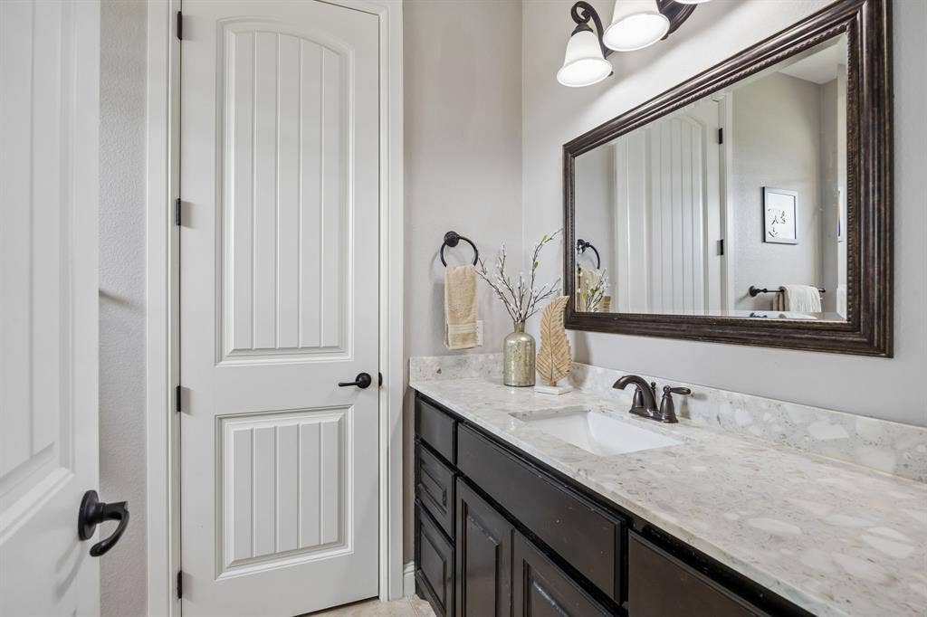 Vanity featuring a stone-composite countertop with an integrated basin, dark-finish cabinetry, a framed wall mirror, and dual-light fixture