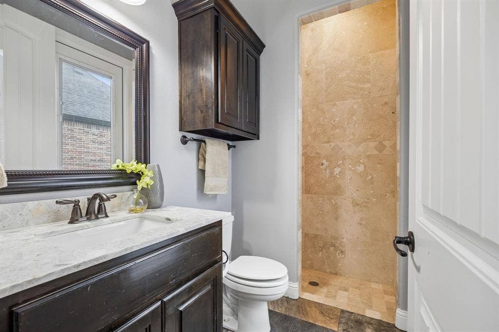 Bathroom featuring a dark wood vanity with a light stone countertop, a framed wall mirror, a matching wall-mounted cabinet, and a walk-in shower with tile surround
