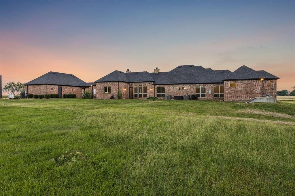Single-story brick exterior featuring a multi-gable roofline, numerous multi-pane windows, and an expansive surrounding lawn