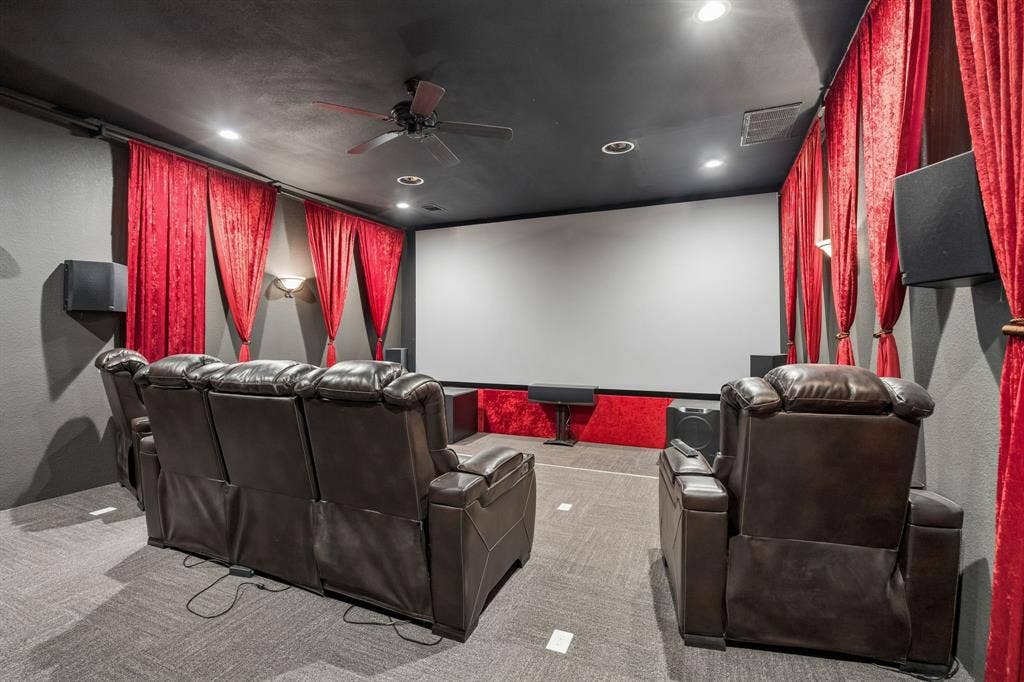 Dedicated detached media room featuring a large-format projection screen, recessed ceiling lighting, a mounted ceiling fan, and wall-mounted sconces