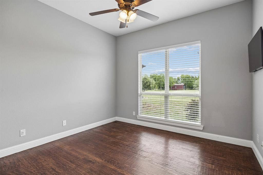 Room featuring wood-finish flooring, neutral wall paint, a multi-blade ceiling fan with integrated lighting, and a large window with horizontal blinds