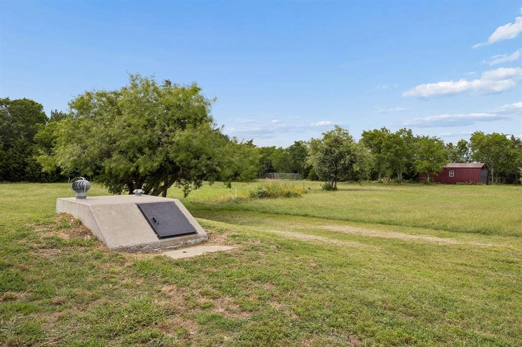 Expansive parcel featuring a concrete storm shelter with a metal access door and turbine vent, mature trees, and a detached storage structure