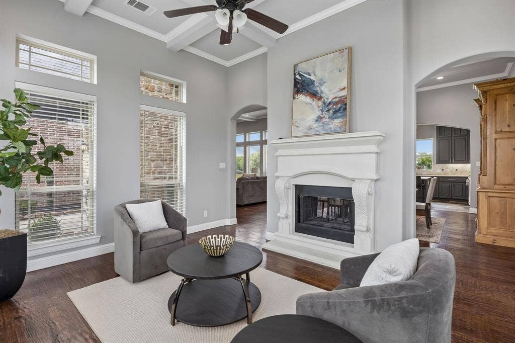 High ceilings featuring coffered detailing, wood-finish flooring, tall windows, and a masonry fireplace with an ornate mantel