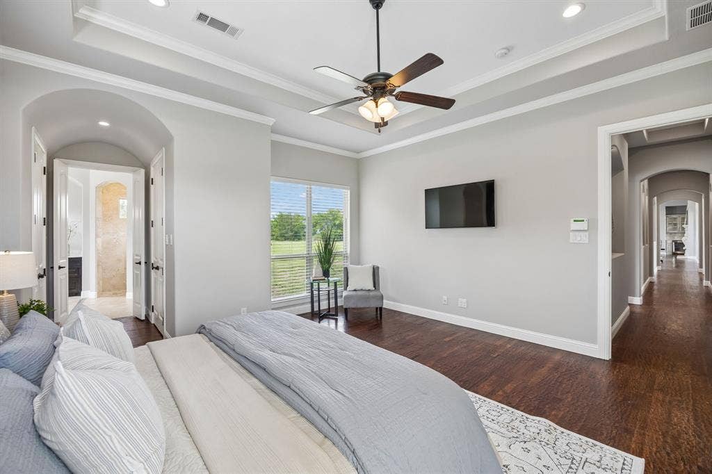 Tray ceiling with a central multi-blade ceiling fan, arched doorways, wood-finish flooring, and natural light from a large window