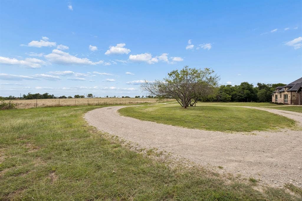 Expansive grounds featuring a circular gravel driveway, mature trees, open pasture, and wire perimeter fencing