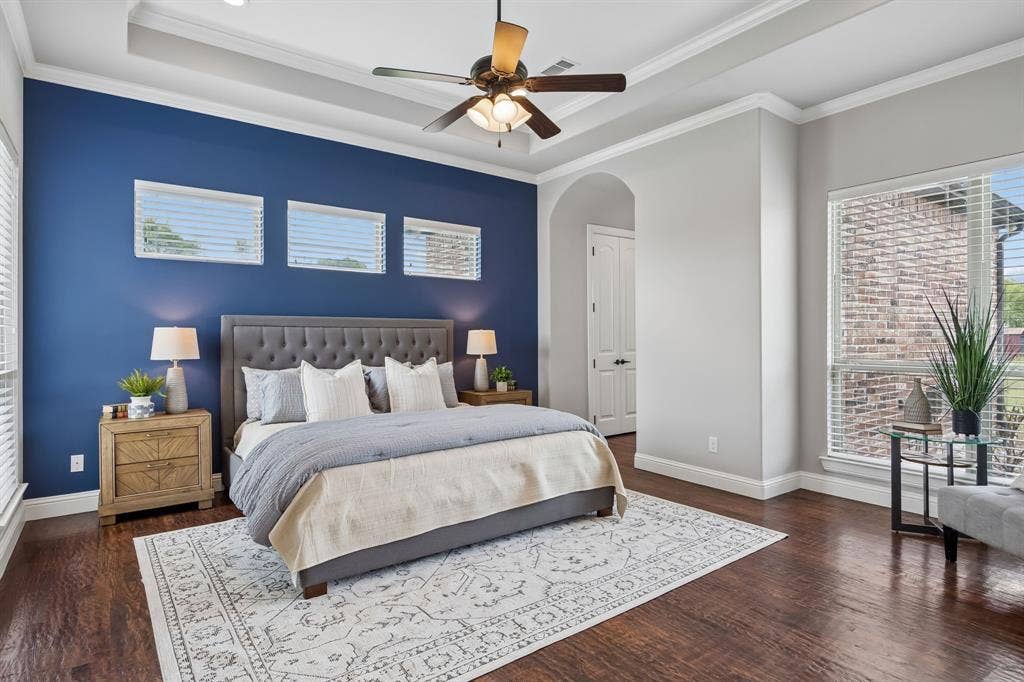Tray ceiling with crown molding, dark wood-finish flooring, accent wall, and ceiling fan with integrated lighting