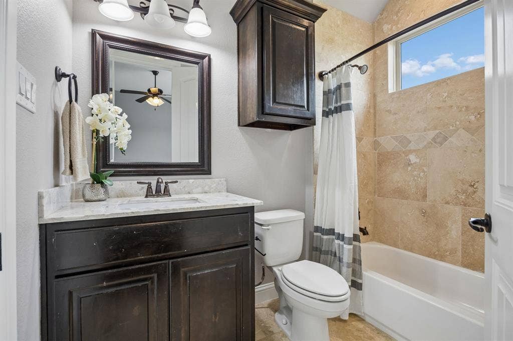 Bathroom featuring a vanity with a light-toned countertop, oil-rubbed bronze fixtures, a wall-mounted dark wood cabinet, and a tiled shower surround with a built-in transom window