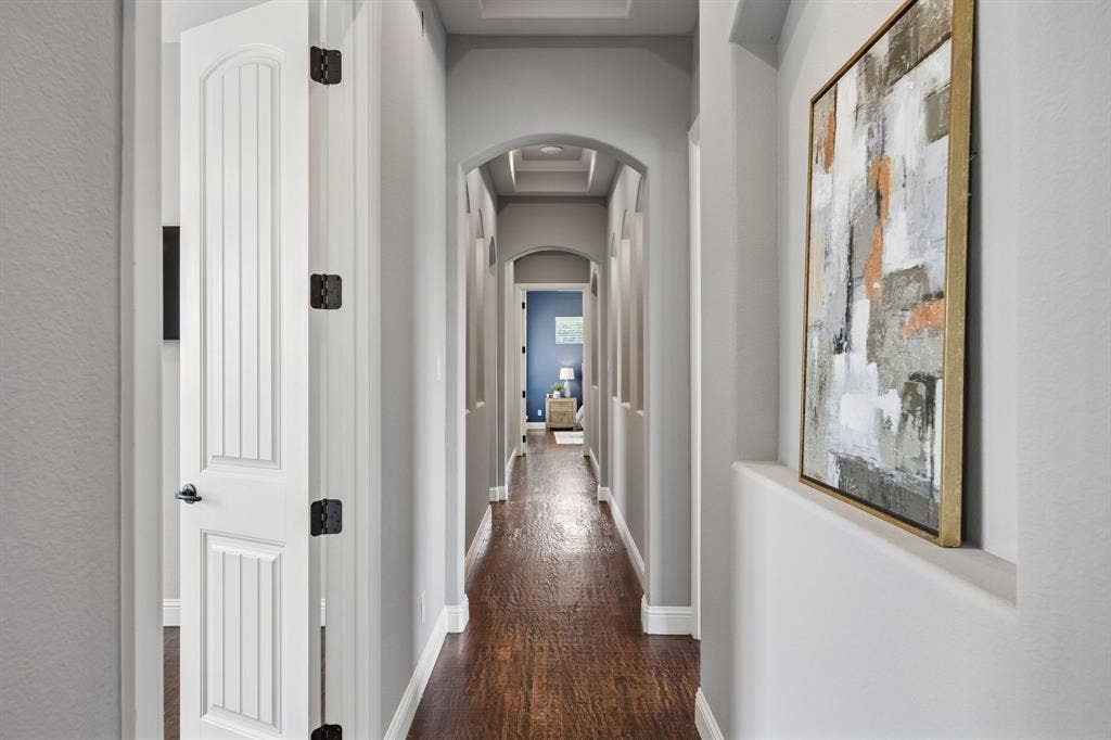 Hallway featuring wood-finish flooring, recessed wall niches, arched architectural detailing, and coffered ceiling elements